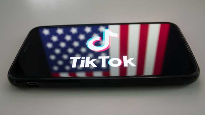 TikTok-Logo auf einem Smartphone, in dem sich die US-Flagge spiegelt.