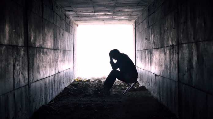 Depressiver Mann in einem Tunnel, an dessen Ende Licht ist