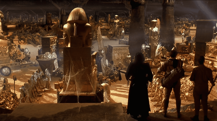 Drei Charaktere des Films "Die Mumie" blicken in einen mit Gold, Statuen und ägyptischen Figuren gefüllten Saal