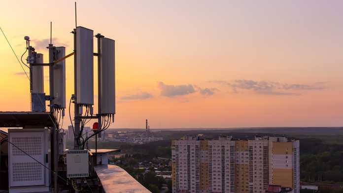 Mobilfunkantennen auf dem Dach eines Wohnblocks mit einem rötlichen Abendhimmel im Hintergrund.