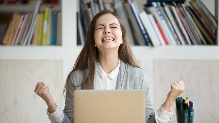 Eine junge Frau in Businesskleidung freut sich vor ihrem Laptop
