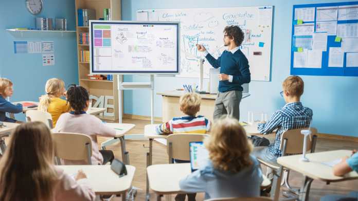 Ein Lehrer steht mit einem Smartboard vor der Klasse