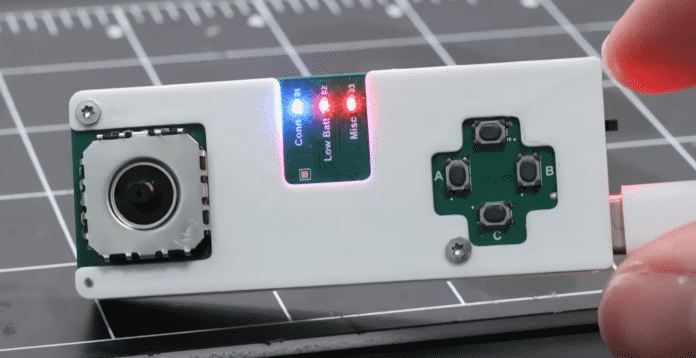 Ein kleiner Controller wird in die Kamera gehalten. Das Gehäuse besteht aus weißem Plastik. Links ist ein Analogstick und rechts vier Buttons aufgetragen.