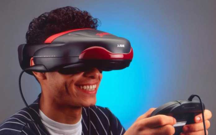 A young man grinning wears VR goggles and holds a controller in his hand.