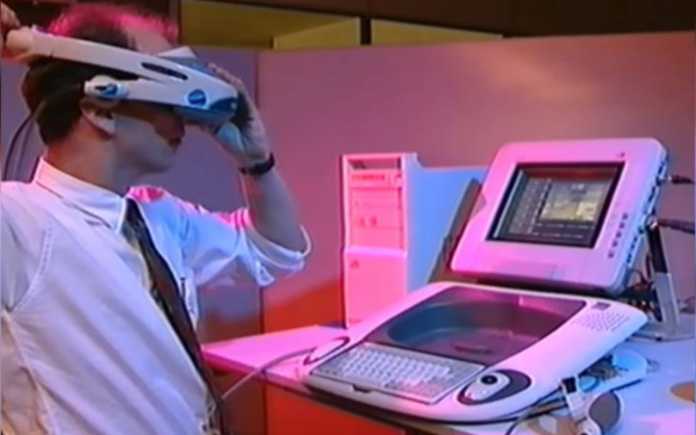 A man sits in an office in front of a workstation wearing white VR glasses.