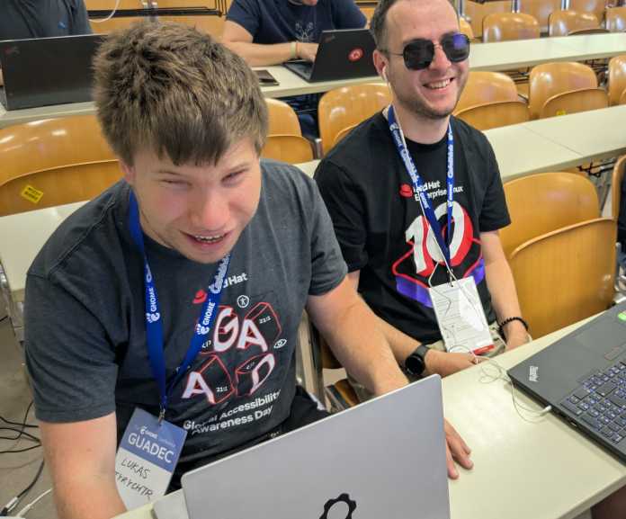 Lukáš Tyrychtr and Vojtěch Polášek, two young men, are sitting in the lecture hall, both smiling and with laptops in front of them.