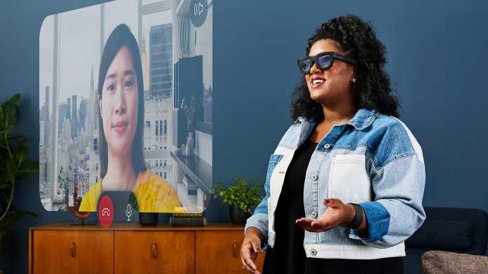 A woman wears Meta's Orion AR glasses and has the window of a video call with her conversation partner superimposed on her field of vision.