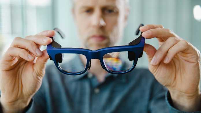 A man holds a pair of glasses with a waveguide display in his hands.