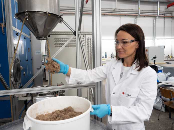 A white woman in a white coat takes brown flakes and puts them in a white plastic bucket