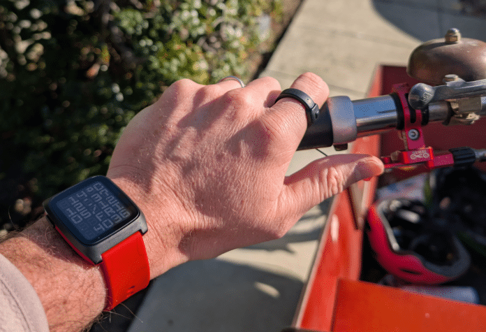 Eine linke Hand mit schwarzem Ring am Zeigefinger lenkt ein Fahrrad