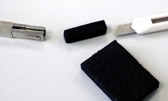 Neben einem quadratischen Pastellkreidenhalter liegt ein passend zugeschnittenes Stück schwarzes Hartgummi.