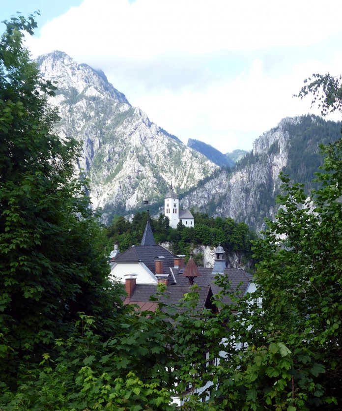 Aussicht auf Dorf mit Kirche auf einem Hügel, dahinter Alpen