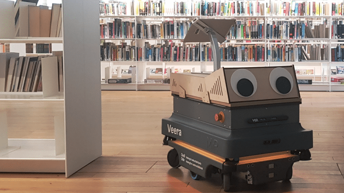 Ein schwarzer Kasten mit Rollen, vorn sind große Kugelaugen befestigt, im Hintergrund sind viele Bücherregale zu sehen.