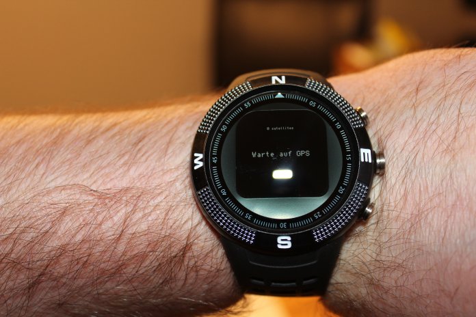 Eine Arm, der eine schwarze Smartwatch am Handgelenk trägt. Auf dem Display steht: Wait for GPS.