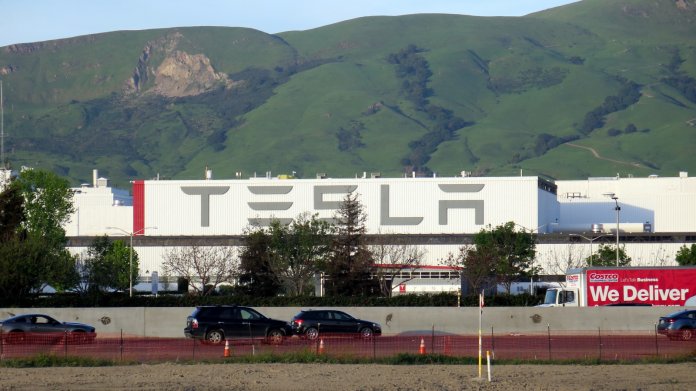Fabrikhalle mit Aufschrift "Tesla", davor eine Autobahn