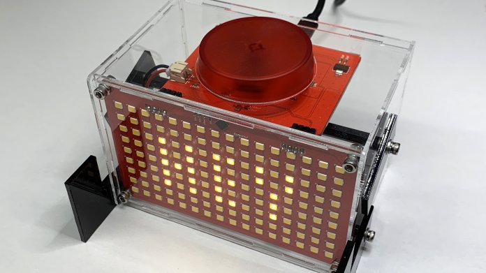 Ein transparenter Acrylkasten. Vorn ist eine LED-Matrix mit der Aufschrift HEY, oben ein roter Button.