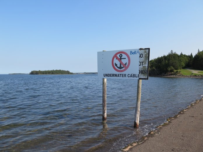 Verbotsschild mit Symbol &quot;ankern verboten&quot; und Aufschrift &quot;Underwater Cable&quot; steht im Meerwasser nahe eines Strandes