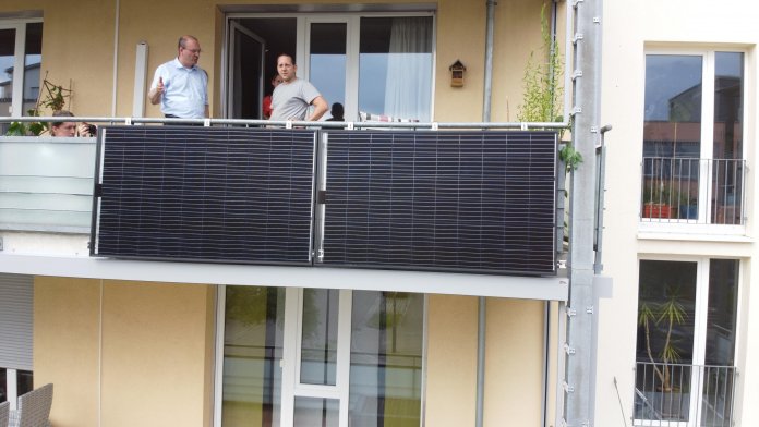 Zwei Personen auf einem Balkon, an dessen Geländer außen Solarmodule befestigt sind.
