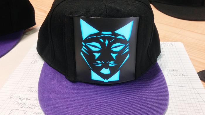 Interaktives Cap mit Arduino: auf einer schwarzen Cap mit lila Schirm ist ein beleuchtetes Motiv, eine stilisierte Katze, angebracht