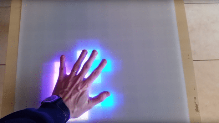 Eine Hand auf einem weißen Ikea-Lack-Tisch. Unter der Hand leuchten LEDs in pink und blau