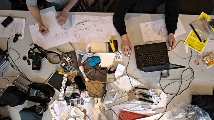 Ein Schreibtisch mit viel Papier, Laptops und vier Händen