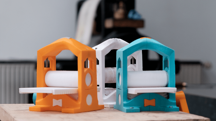 Drei kleine, bunte Druckerpressen aus dem 3D-Drucker, im Hintergrund eine große alte Presse