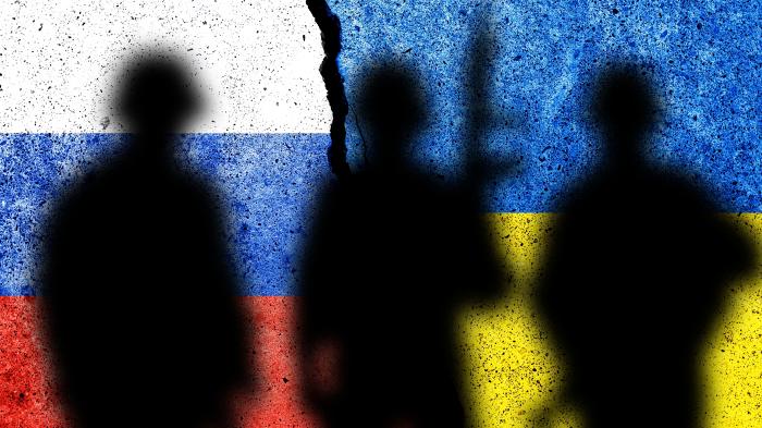Der Schatten von Soldaten vor dem Hintergrund russischer und ukrainischer Flaggen.