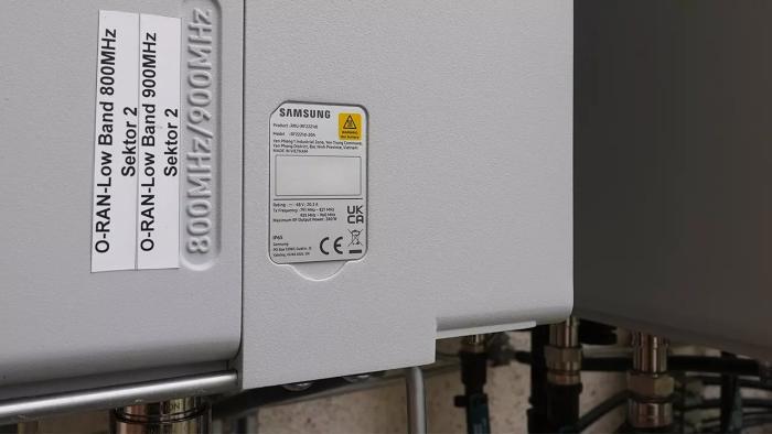 Nahaufnahme eines grauen Kastens mit herausführenden Kabeln, der Mobilfunk-Hardware von Samsung enthält.