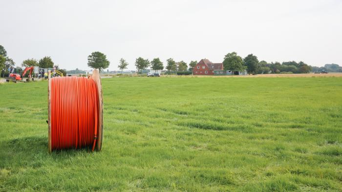 Eine große Kabeltrommel mit orangefarbenem Kabel steht auf einer günen Wiese