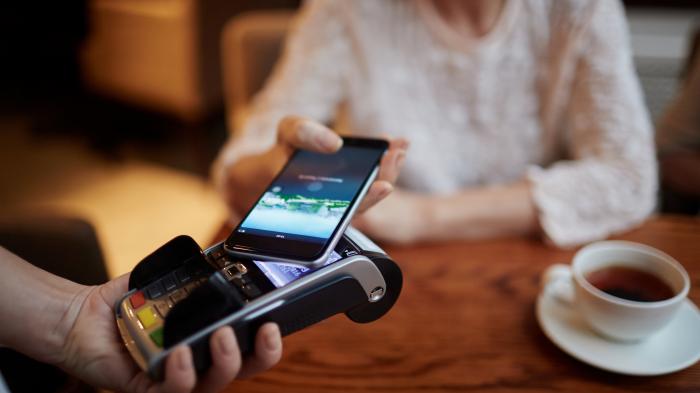 Person holds iPhone to checkout terminal.