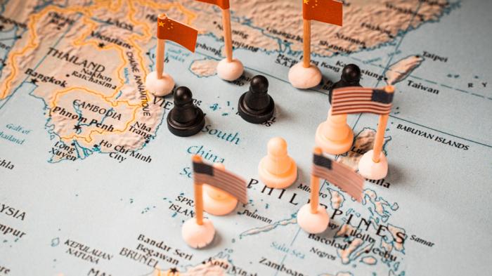 Zu sehen ist eine Karte des Südchinesischen Meeres mit Flaggen von China und den USA sowie schwarzen Figursteinchen