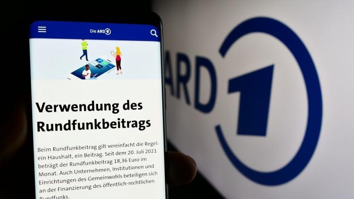 Person hält Smartphone mit Web-Seite des öffentlich-rechtlichen Rundfunks ARD vor Logo.