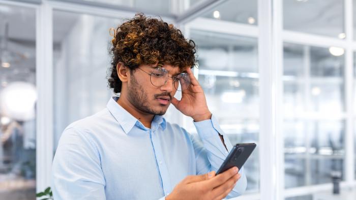 Mann schaut während der Arbeit verärgert auf sein Smartphone.