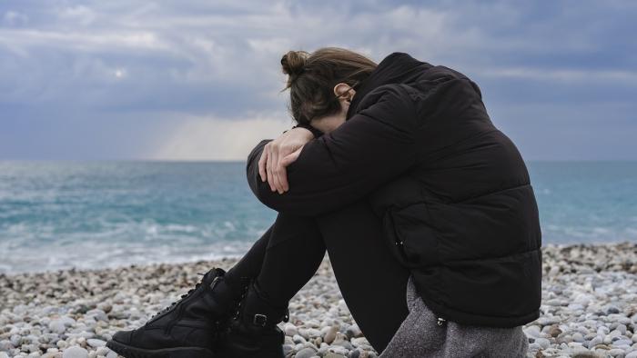 Symbolbild; Traurige junge Frau kauert am Strand