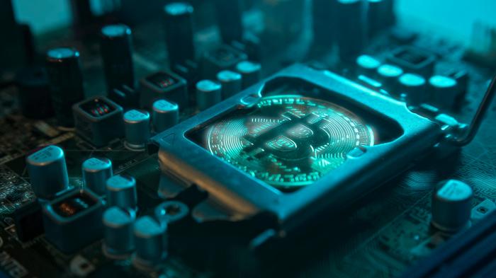 Eine goldene Bitcoin-Münze mit Drüse und Reflektion, die anstelle eines Zentralprozessors in der Hauptplatine mit elektronischen Komponenten mit blauem Licht und Rauch im Dunkeln installiert ist. 