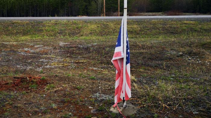 Eine US-Fahne hängt lahm am unteren Ende einer Fahnenstange und somit im nassen Erdreich