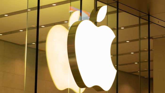 Apple-Logo aus weißem Leuchtzeichen hinter Glasfassade eines Stores.