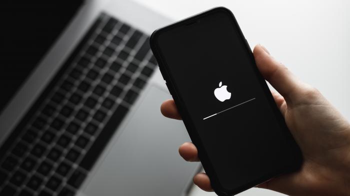 Eine Hand hälte ein iPhone, darunter steht ein geöffnetes MacBook