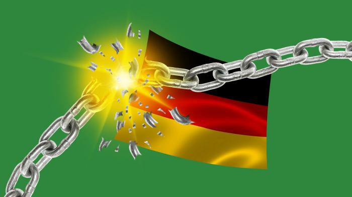 Eine zerbrochene Kette vor der deutschen Flagge mit einem hellen Lichtstrahl