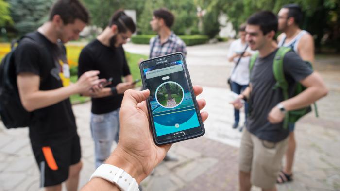 Eine Person hält ein Smartphone, das eine App mit einer Karte und einem Denkmal anzeigt.