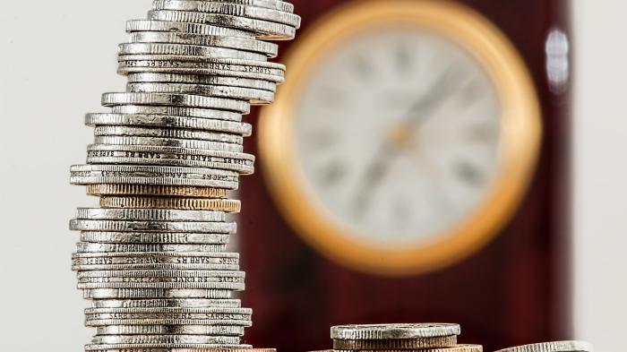 Ein Stoß Münzen, dahinter unscharf eine Uhr