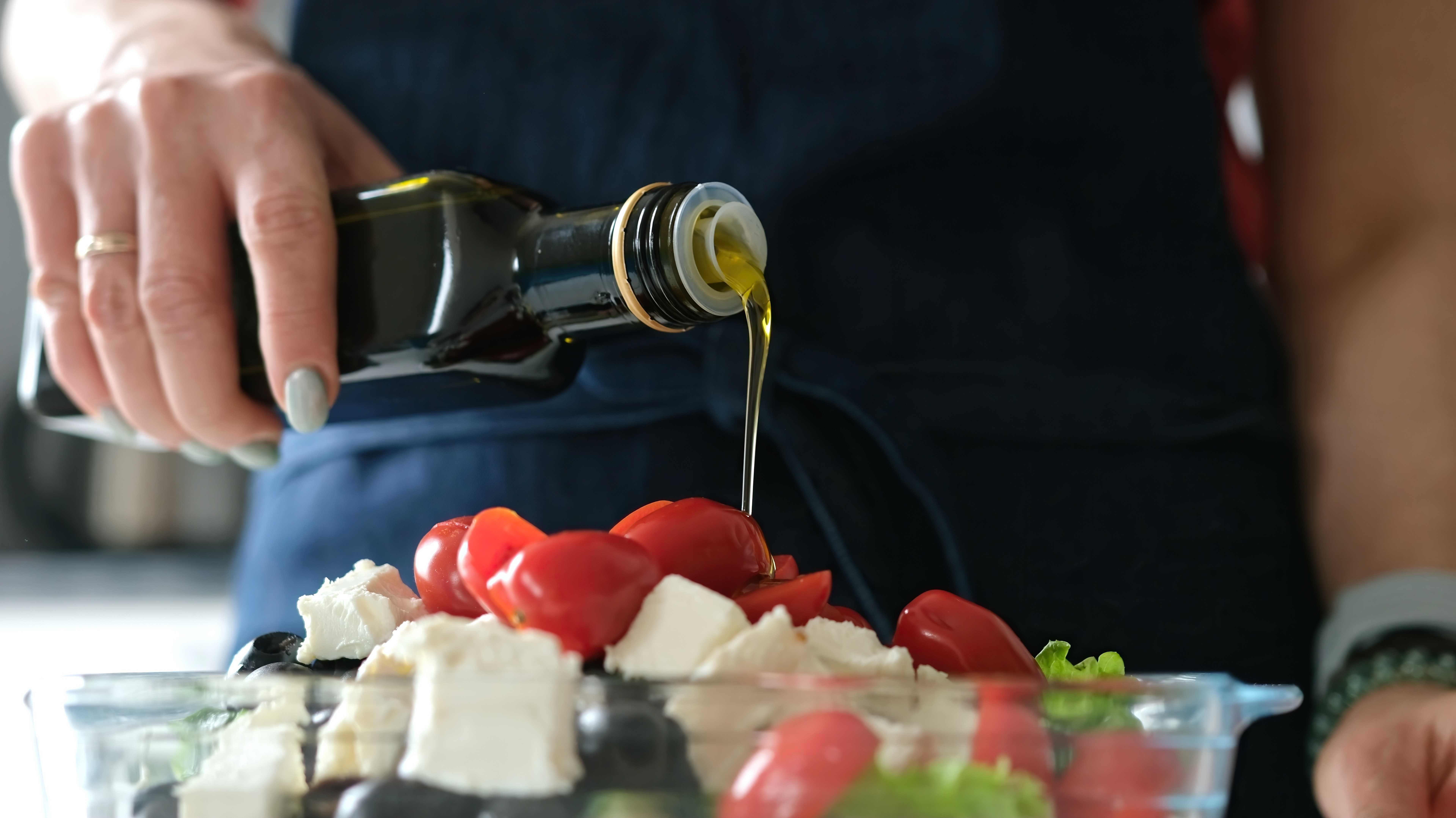 Eine Frau bereitet einen Salat mit Oliven, Tomaten, Feta-Käse und Olivenöl zu. Das gehört zur Mediterranen Diät.